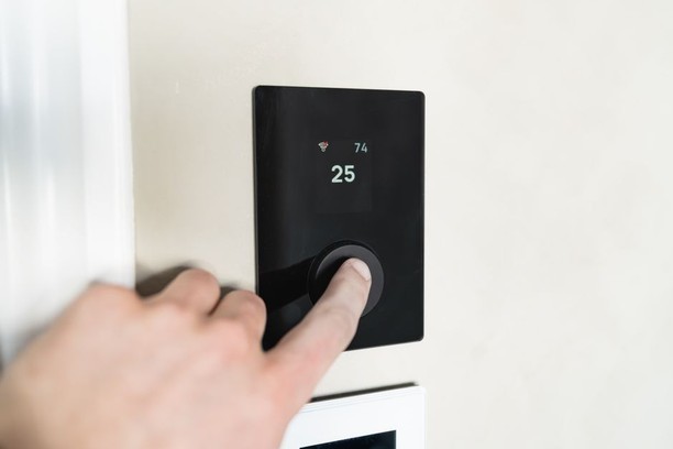 Homeowner adjusting a modern thermostat to maintain indoor air quality